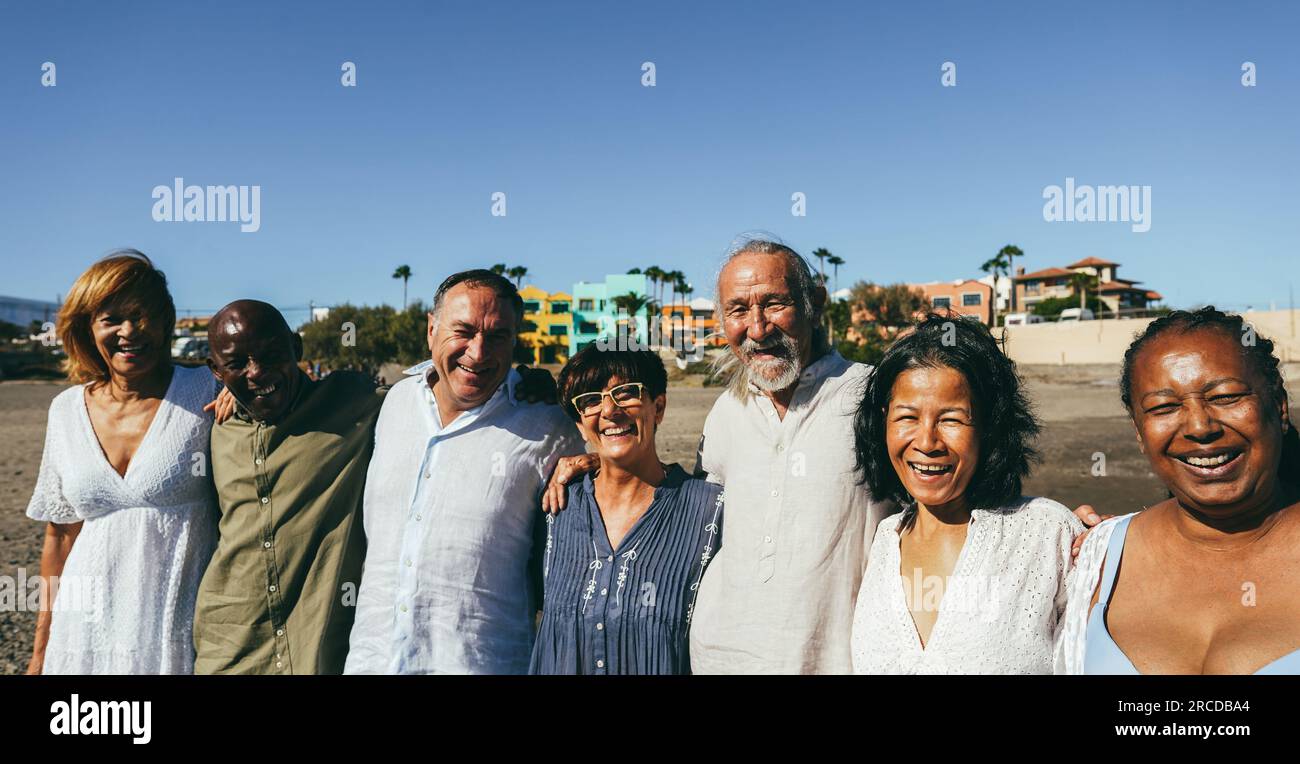 Happy senior people having fun walking on the beach at sunset wearing summer clothes - Joyful elderly lifestyle, pensioner vacation and travel concept Stock Photo