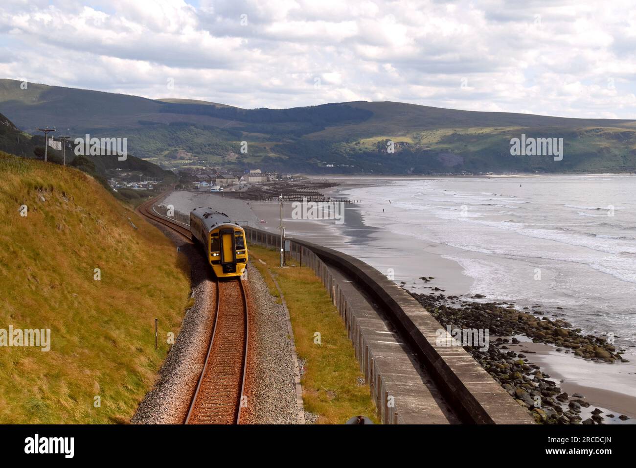 A Transport for Wales DMU train leaving Barmouth by the beach and ...