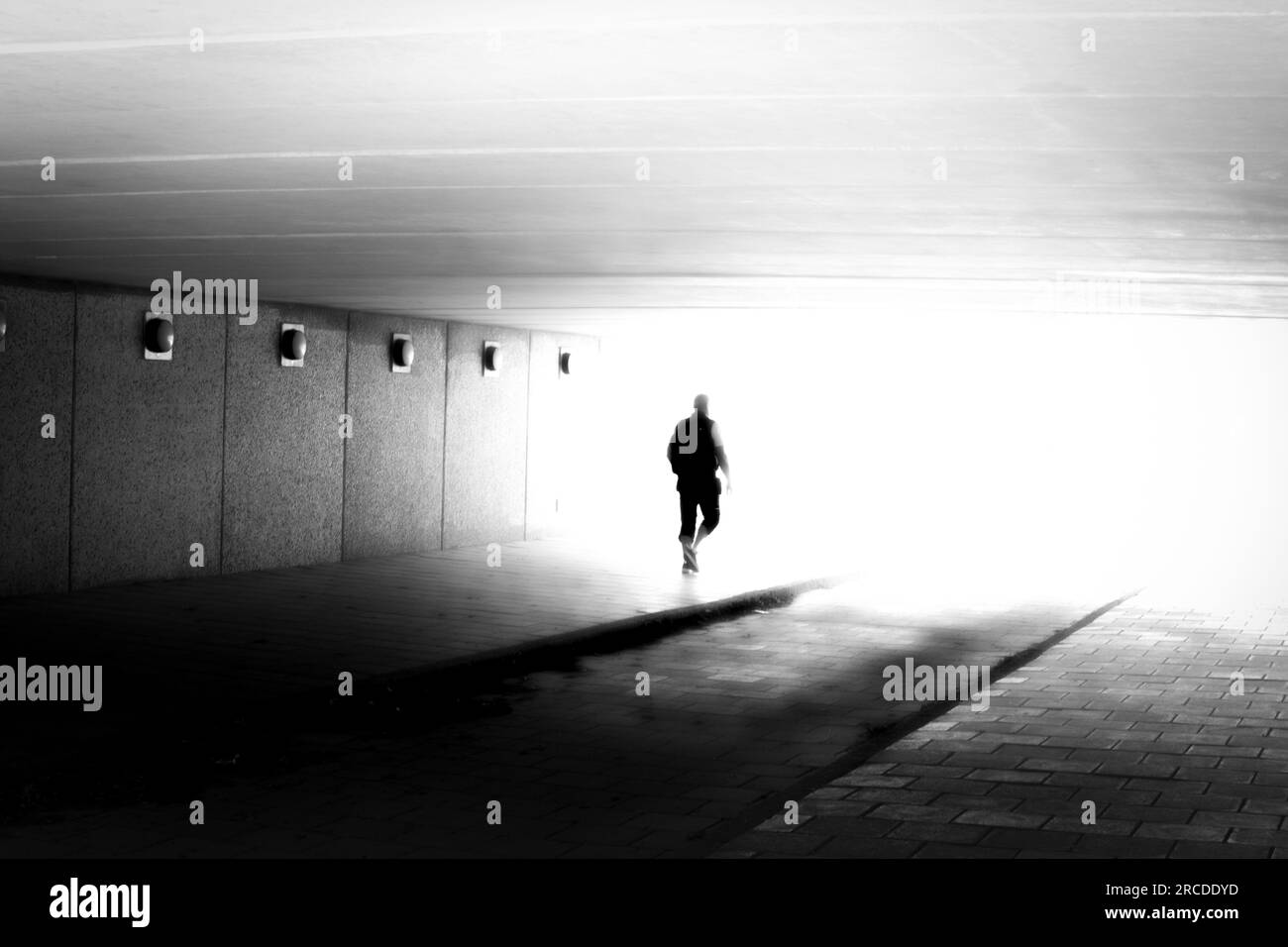 Unrecognizable silhouette of man in motion blur walking in to the light in black and white Stock Photo