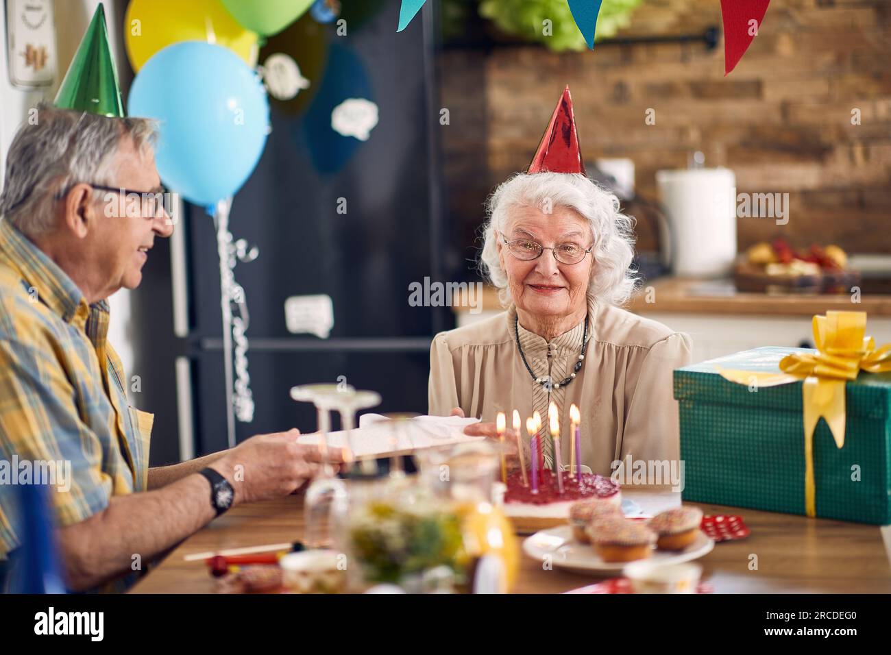 Beautiful happy senior couple sitting at kitchen table in birthday hats ...