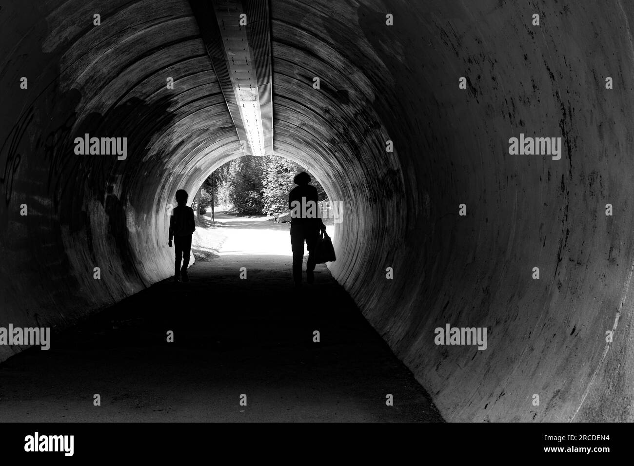 Grandmother and child in silhouettes in tunnel with dog waiting on the other side. Stock Photo