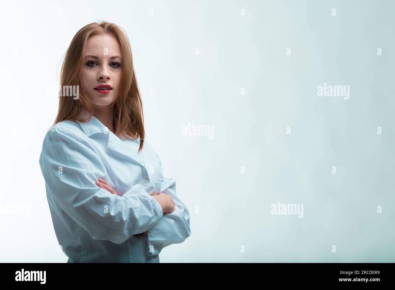 Cross-armed woman in lab coat. She smiles without her eyes. Her reddish-blonde hair signifies the contributions of intelligent, tenacious women in sci Stock Photo