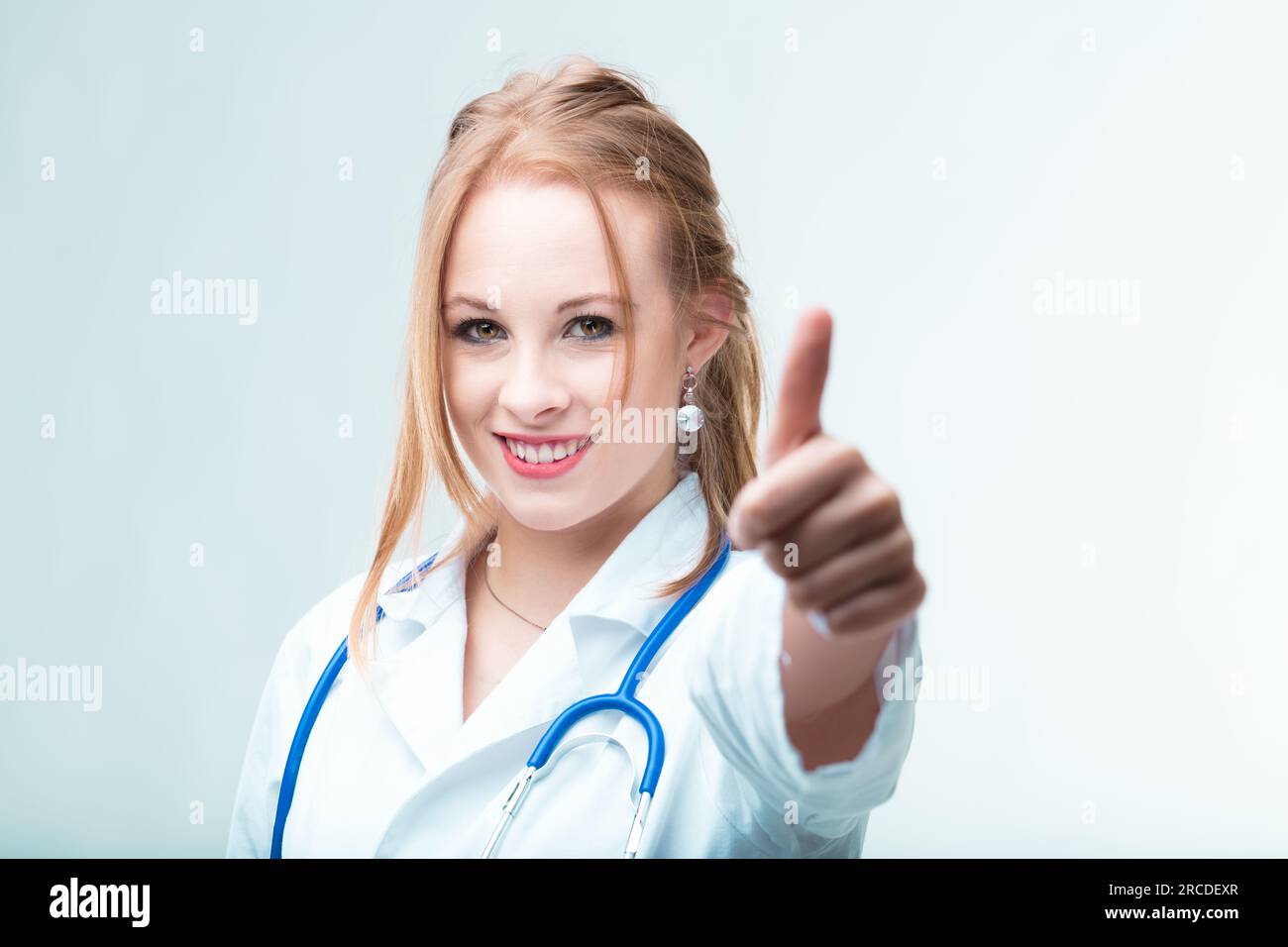 Medicine's good! Treatments are fine! Insurances sorted! Young, cheerful doctor giving thumbs-up assures all will be well Stock Photo