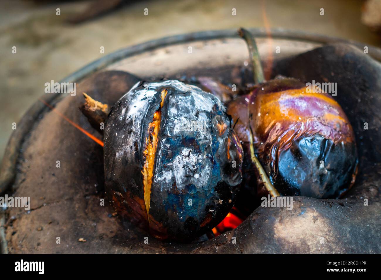 Whole roasted eggplant or brinjal in a traditional clay stove, Angeethi in Northern India. Preparation of a North Indian cuisine, Baigan ka Bharta. In Stock Photo