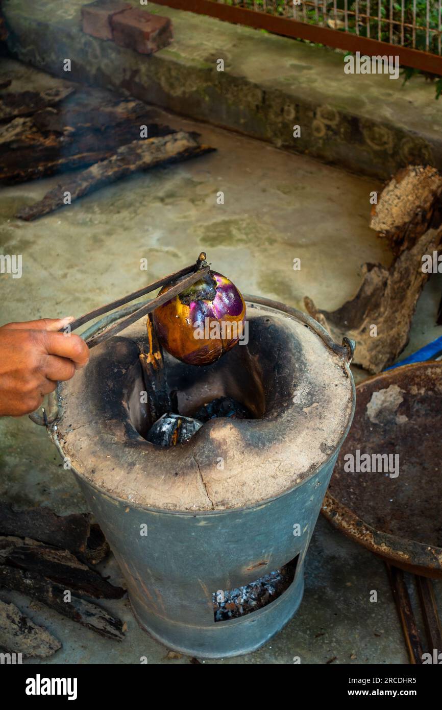 Whole roasted eggplant or brinjal in a traditional clay stove, Angeethi in Northern India. Preparation of a North Indian cuisine, Baigan ka Bharta. In Stock Photo