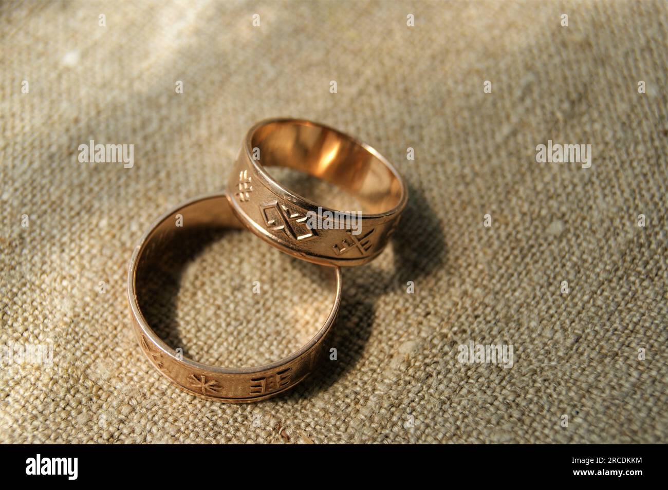 Gold wedding rings with ancient symbols. Rings on linen fabric. Latvian ancient symbols. Stock Photo