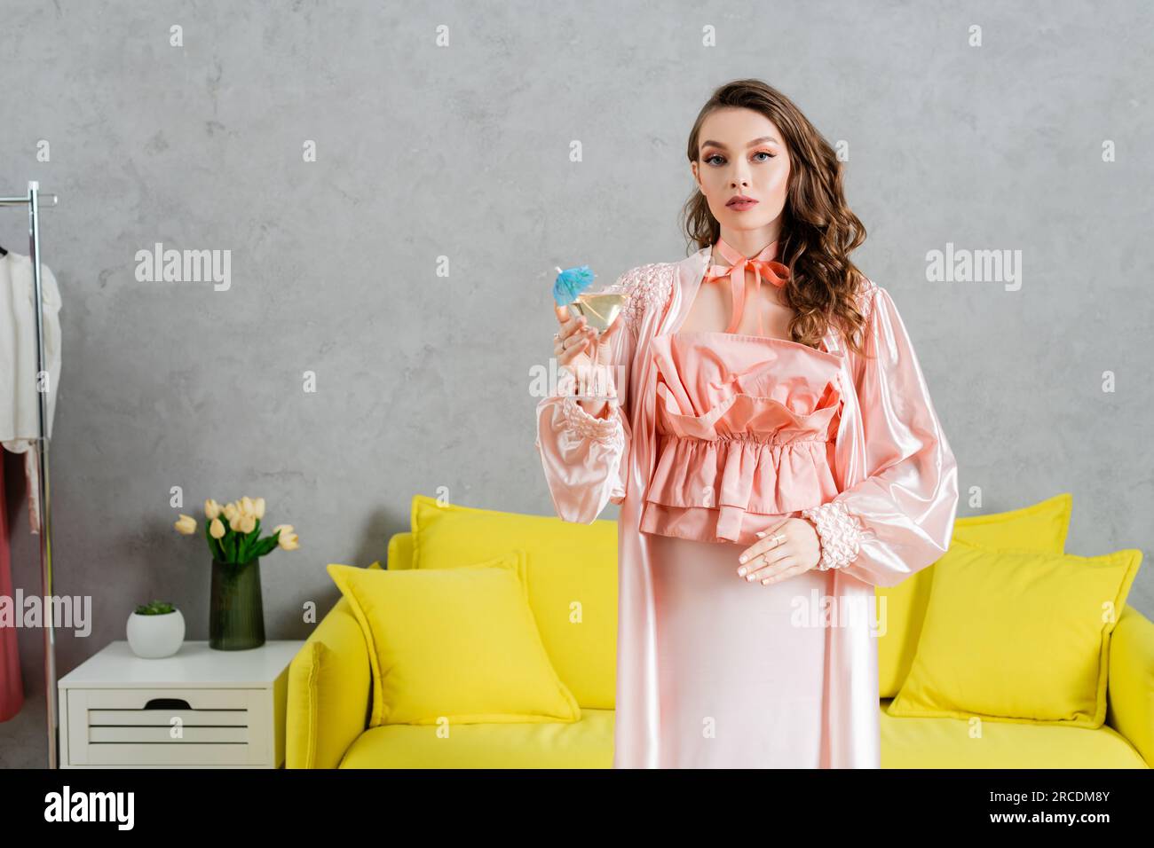 concept photography, woman acting like a doll, domestic life, housewife in pink outfit with silk robe holding cocktail in glass, gesturing and standin Stock Photo