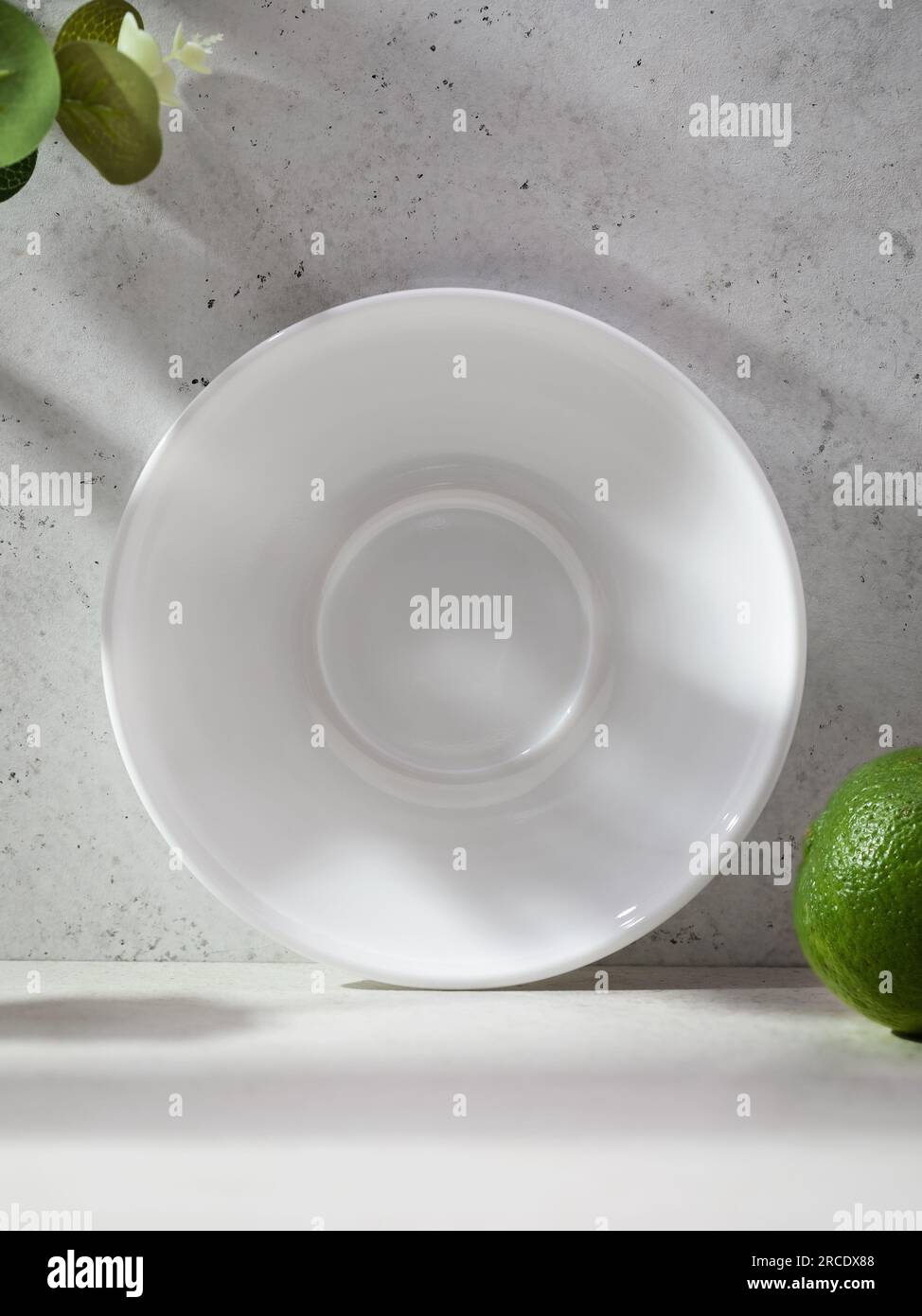 White ceramic plate on an abstract background surrounded by flowers and lime Stock Photo