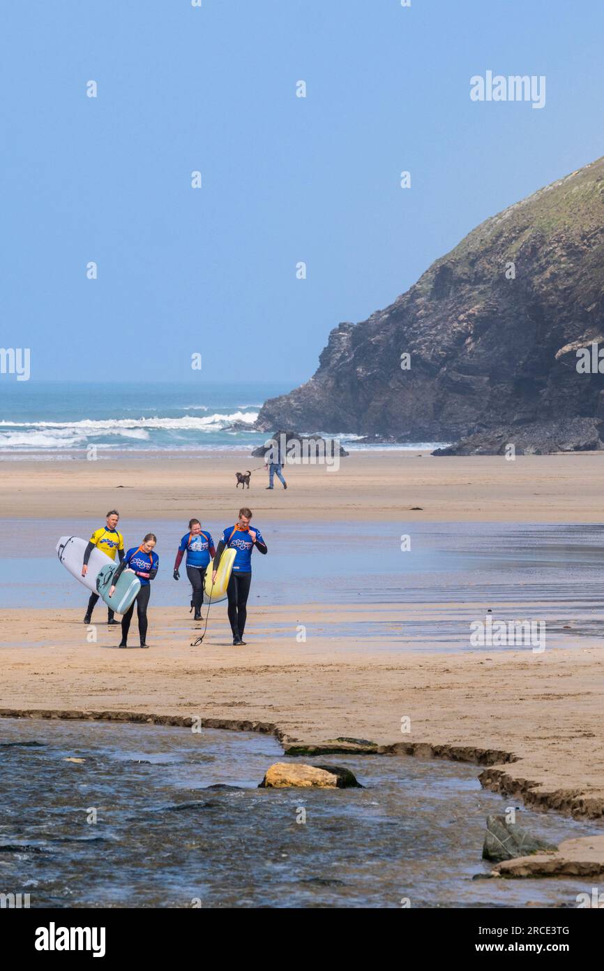 Three surfers and their surfing instructor carrying their surfboards and walking after a surfing