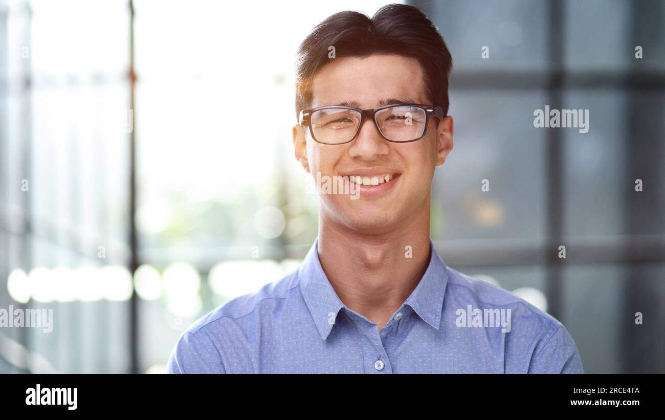Well dressed young Asian businessman smiling confidently while standing alone in a bright modern office Stock Photo