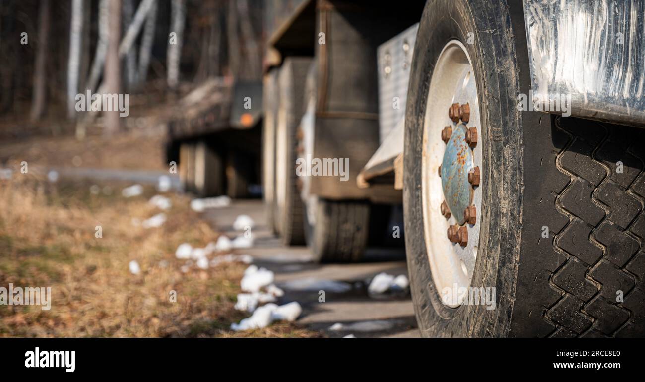 Front tire and wheel of a truck and trailer parked on a paved road on a sunny afternoon, with melting chunks of snow on the ground at job site. Shallo Stock Photo