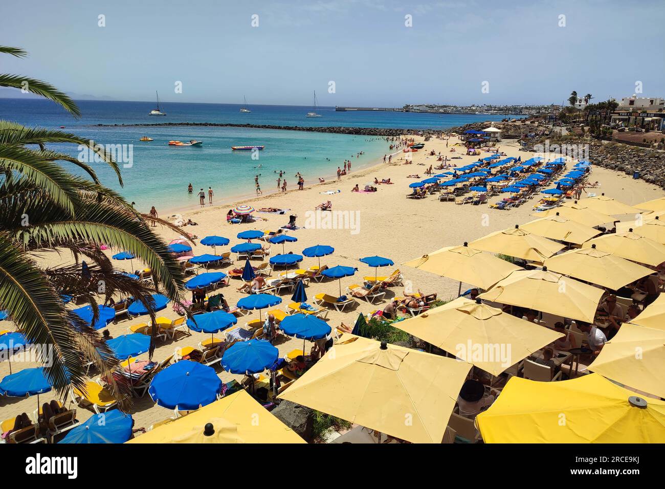 Playa Blanca, Lanzarote 14th July 2023. Sunseekers flocked to the beach at the resort of Playa Blanca as scorching conditions continued to batter Spain. Both British tourists and other nationalities cowered under parasols and enjoyed a strong, if not very warm sea breeze. The popular Lanzarote destination on the south of the Spanish island in the Canaries boasts white sand and crystal clear waters. Credit: Stop Press Media/Alamy Live News Stock Photo