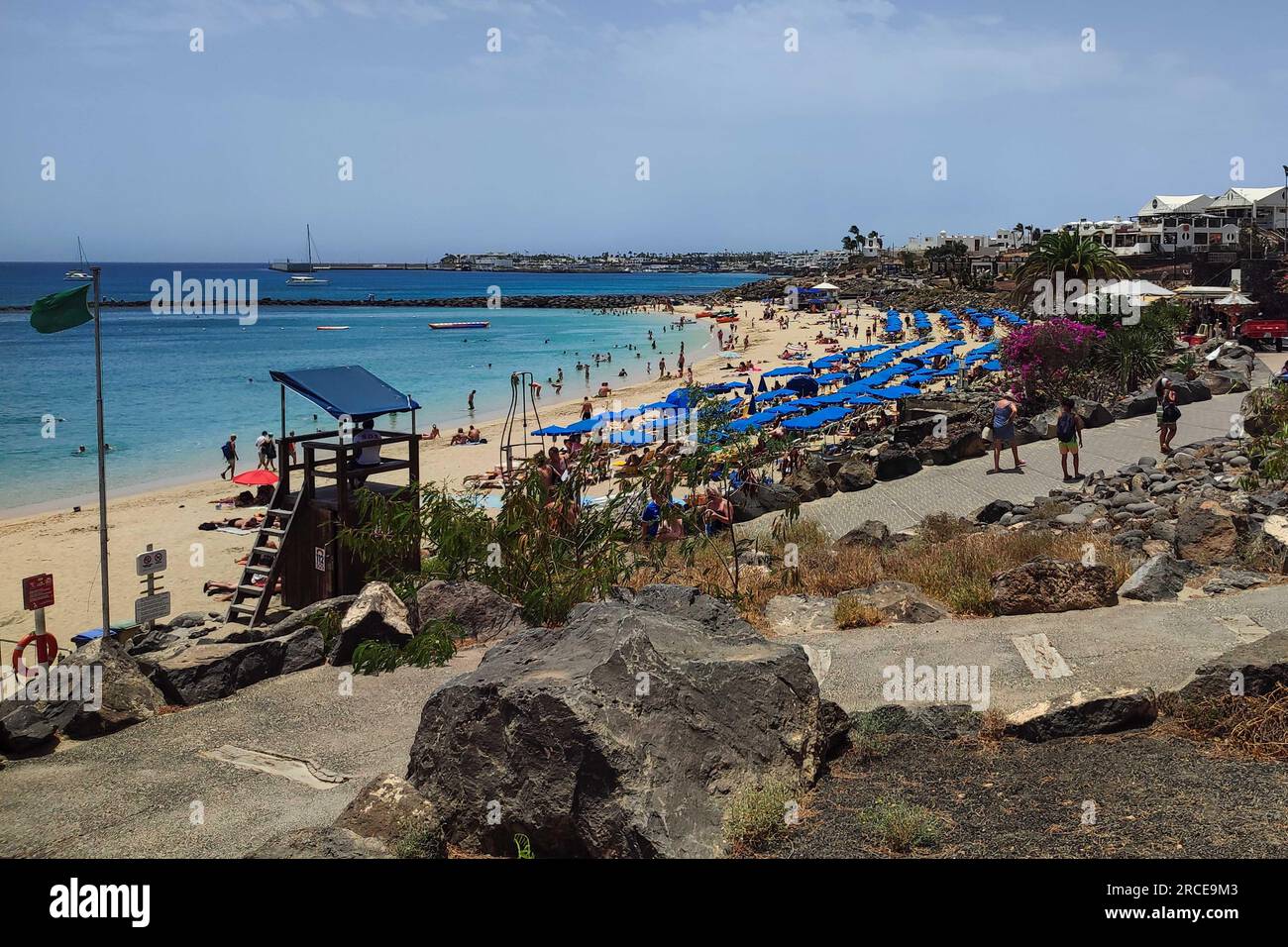 Playa Blanca, Lanzarote 14th July 2023. Sunseekers flocked to the beach at the resort of Playa Blanca as scorching conditions continued to batter Spain. Both British tourists and other nationalities cowered under parasols and enjoyed a strong, if not very warm sea breeze. The popular Lanzarote destination on the south of the Spanish island in the Canaries boasts white sand and crystal clear waters. Credit: Stop Press Media/Alamy Live News Stock Photo