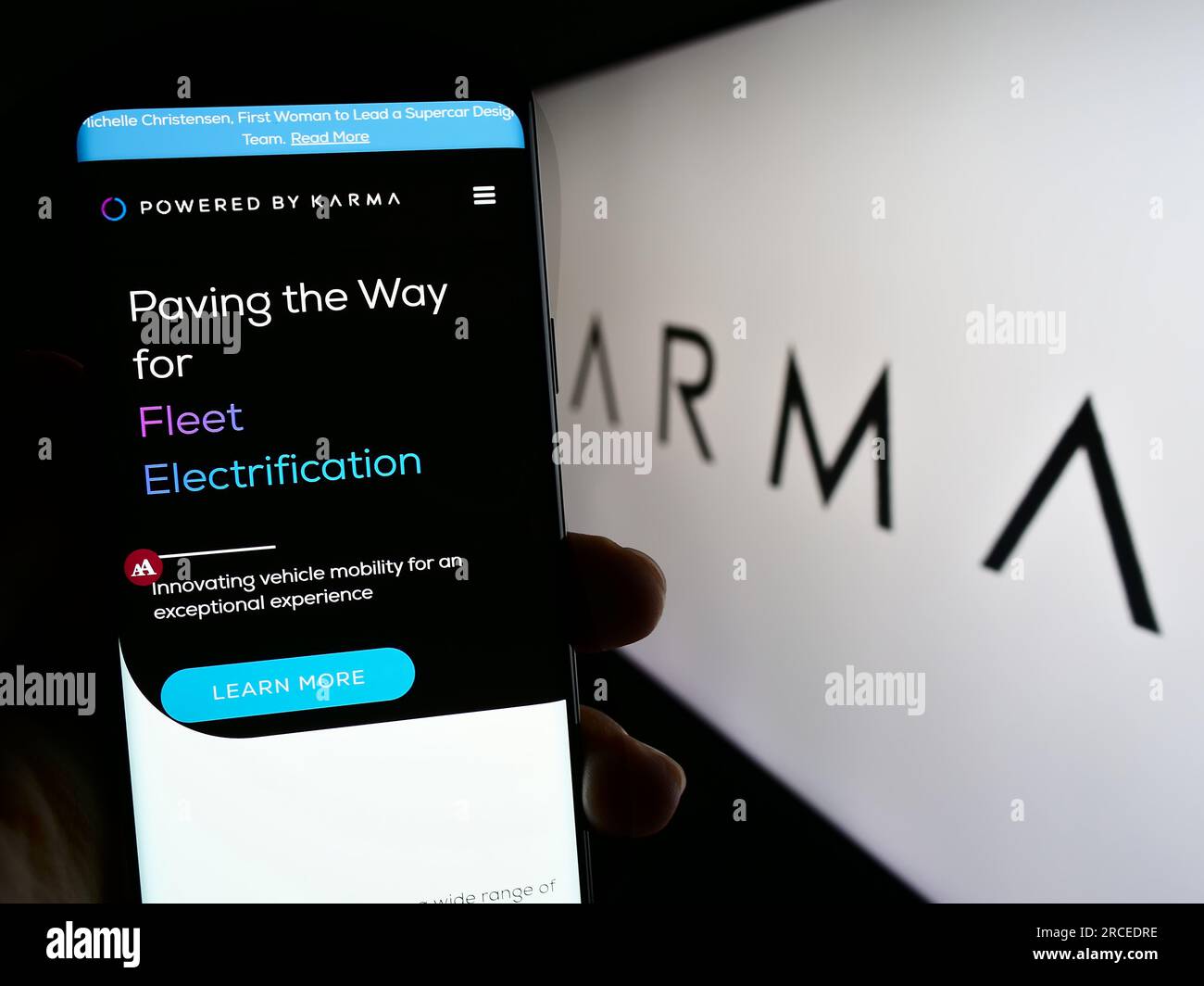 Person holding cellphone with website of electric vehicle company Karma Automotive LLC on screen with logo. Focus on center of phone display. Stock Photo