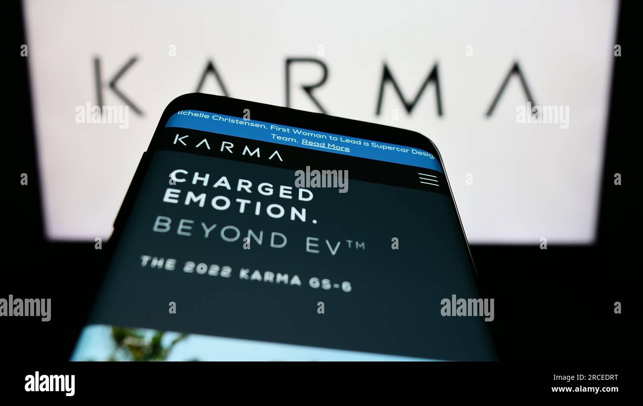 Mobile phone with webpage of electric vehicle company Karma Automotive LLC on screen in front of logo. Focus on top-left of phone display. Stock Photo