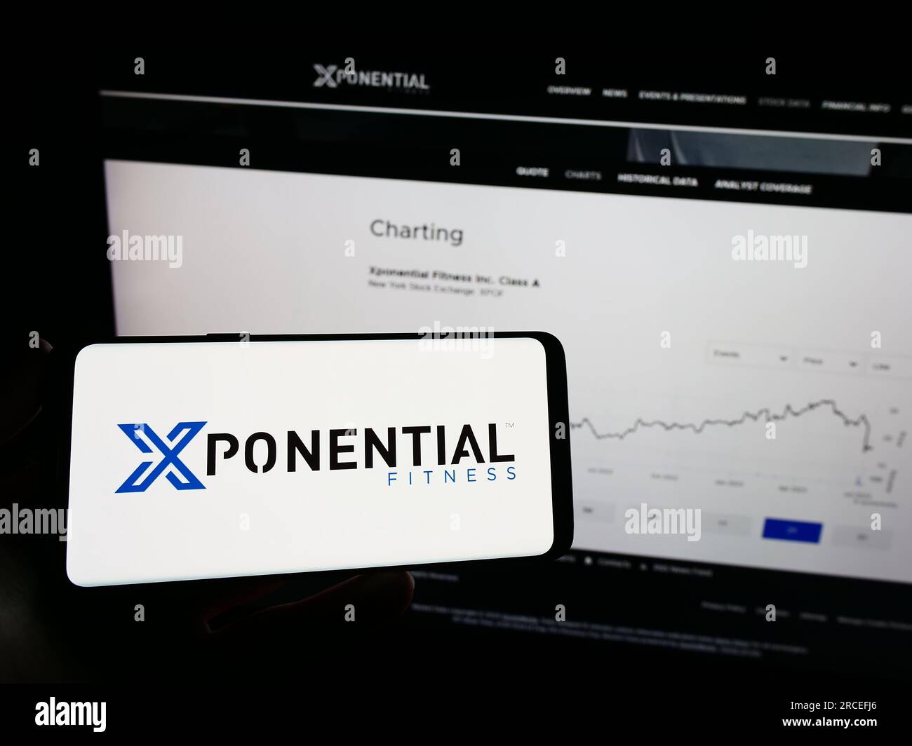 Person holding mobile phone with logo of US franchise company Xponential Fitness Inc. on screen in front of web page. Focus on phone display. Stock Photo