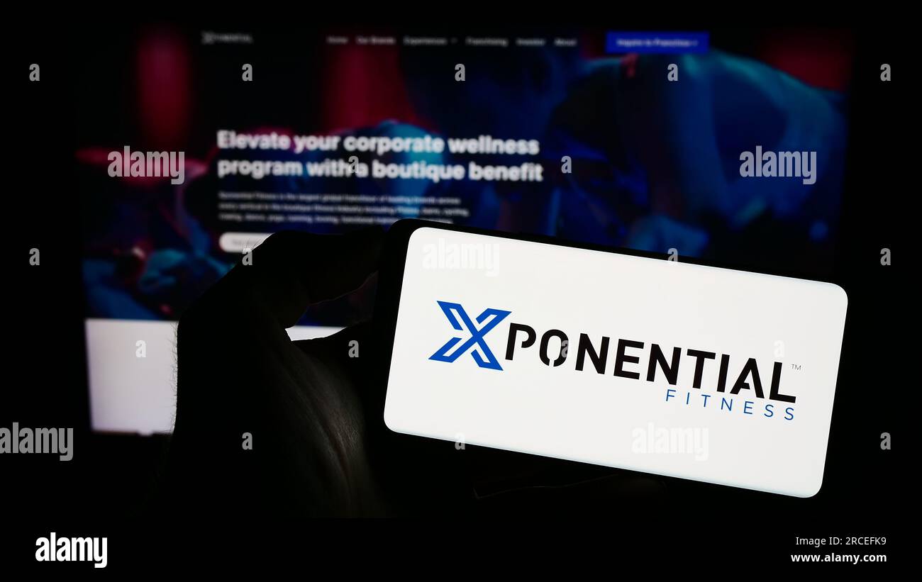 Person holding smartphone with logo of US franchise company Xponential Fitness Inc. on screen in front of website. Focus on phone display. Stock Photo