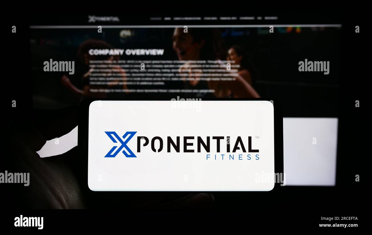Person holding cellphone with logo of American franchise company Xponential Fitness Inc. on screen in front of webpage. Focus on phone display. Stock Photo