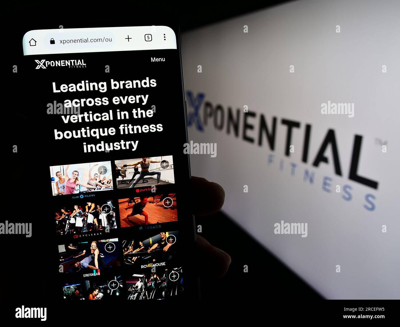 Person holding mobile phone with webpage of US franchise company Xponential Fitness Inc. on screen with logo. Focus on center of phone display. Stock Photo