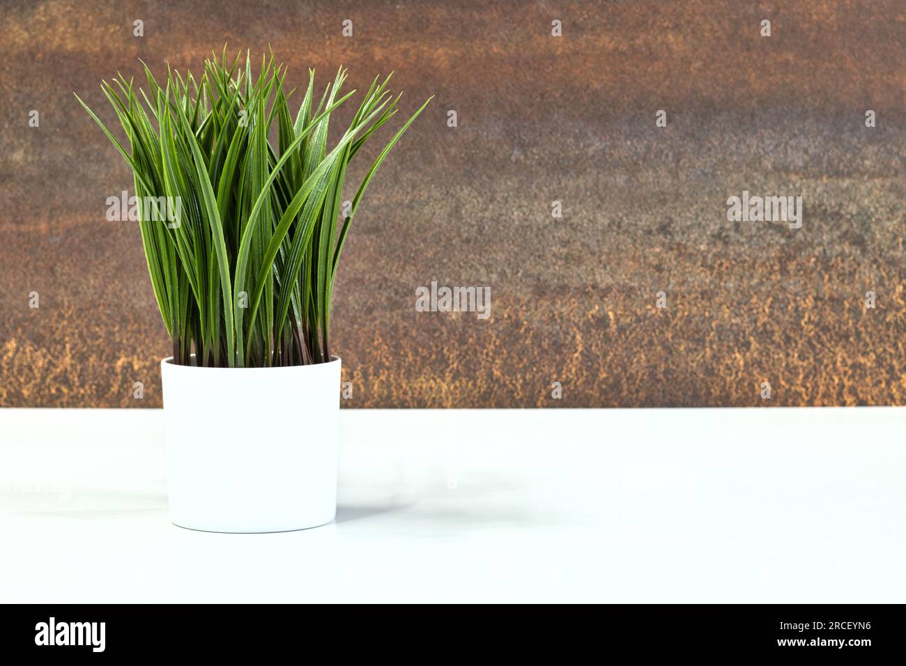 Contemporary interior design, artificial decorative potted plant on a white partial table and brown defocused feature wall. Stock Photo