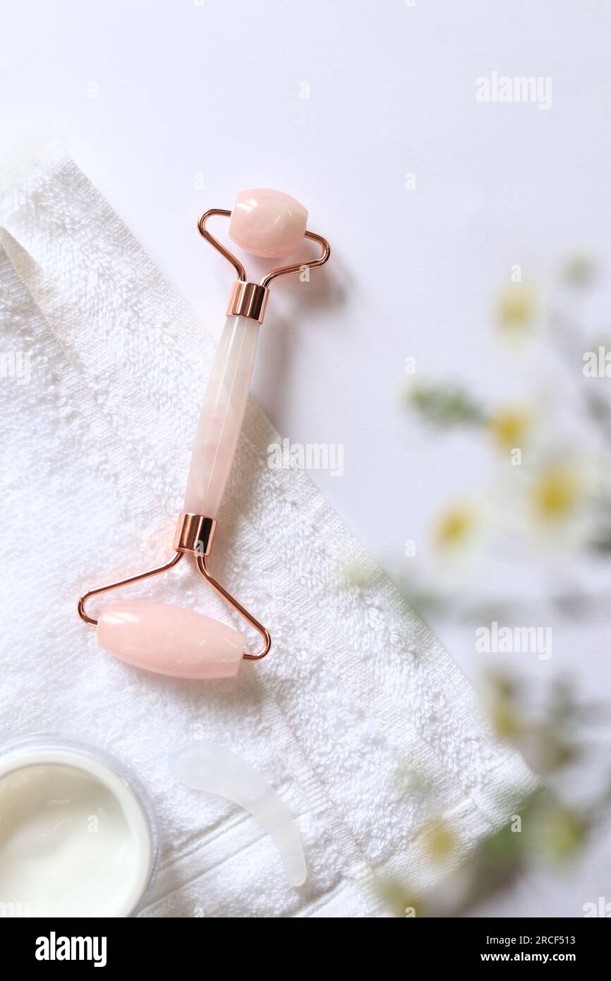 Rose quartz facial roller. Roller for cosmetic facial massage, cream and towel. Flat lay on a light background Stock Photo