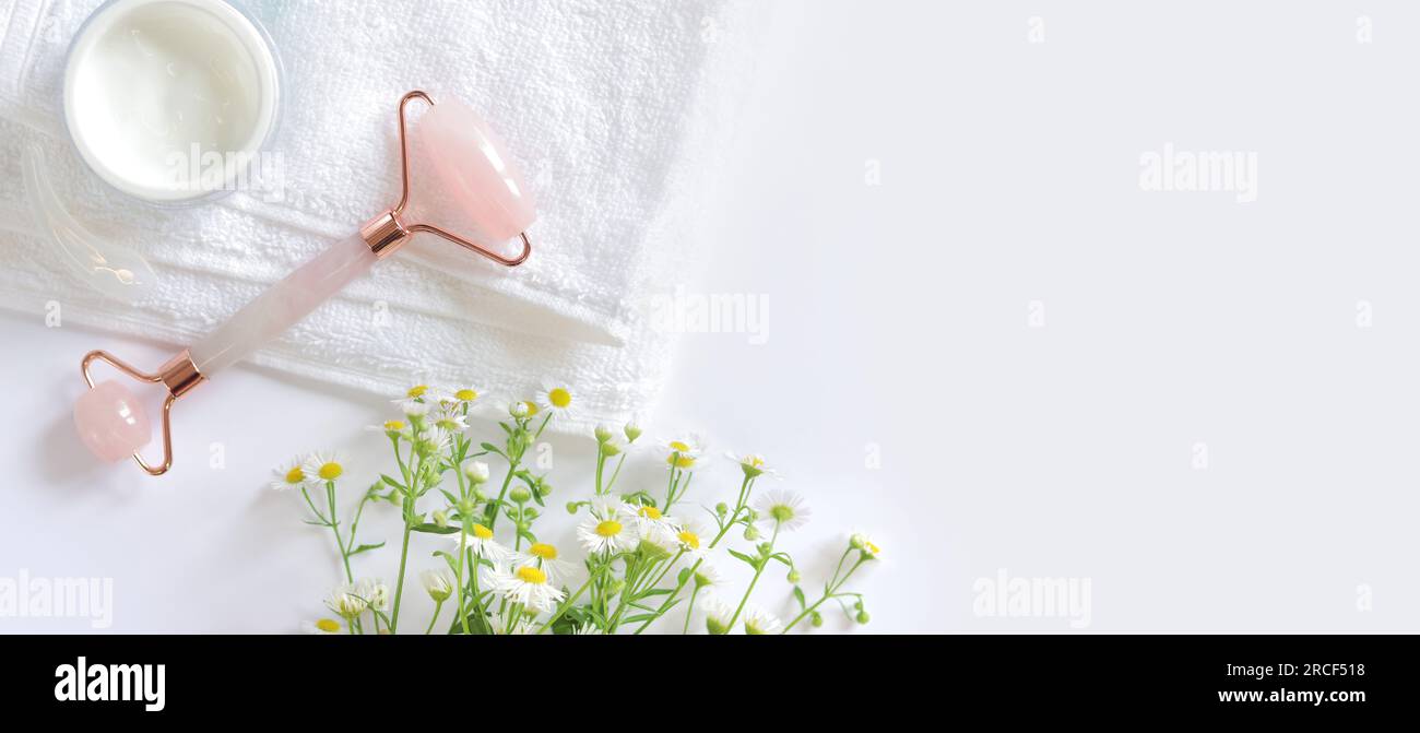 Rose quartz facial roller. Roller for cosmetic facial massage, cream, chamomile and towel. Flat lay on a light background. Top view, copy space Stock Photo