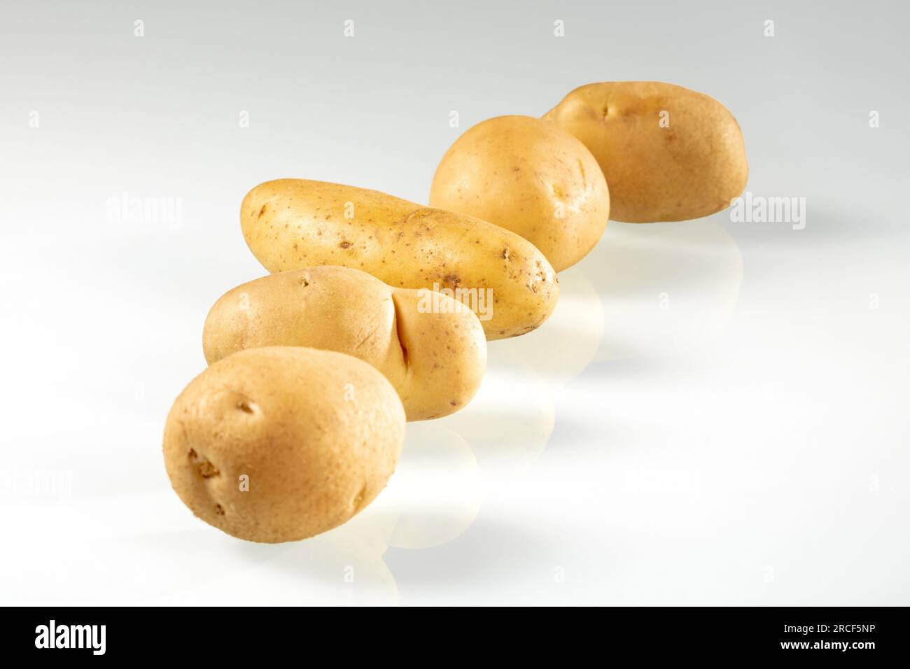 Tubers of young potatoes lie in a row on a white background. Stock Photo