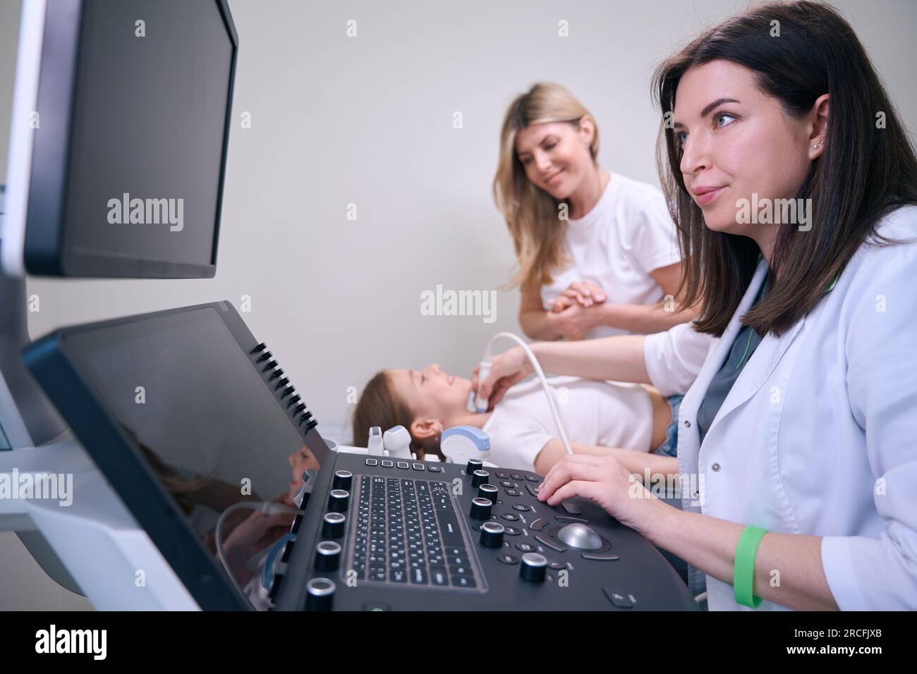Female blonde with her daughter for ultrasound of thyroid gland stock