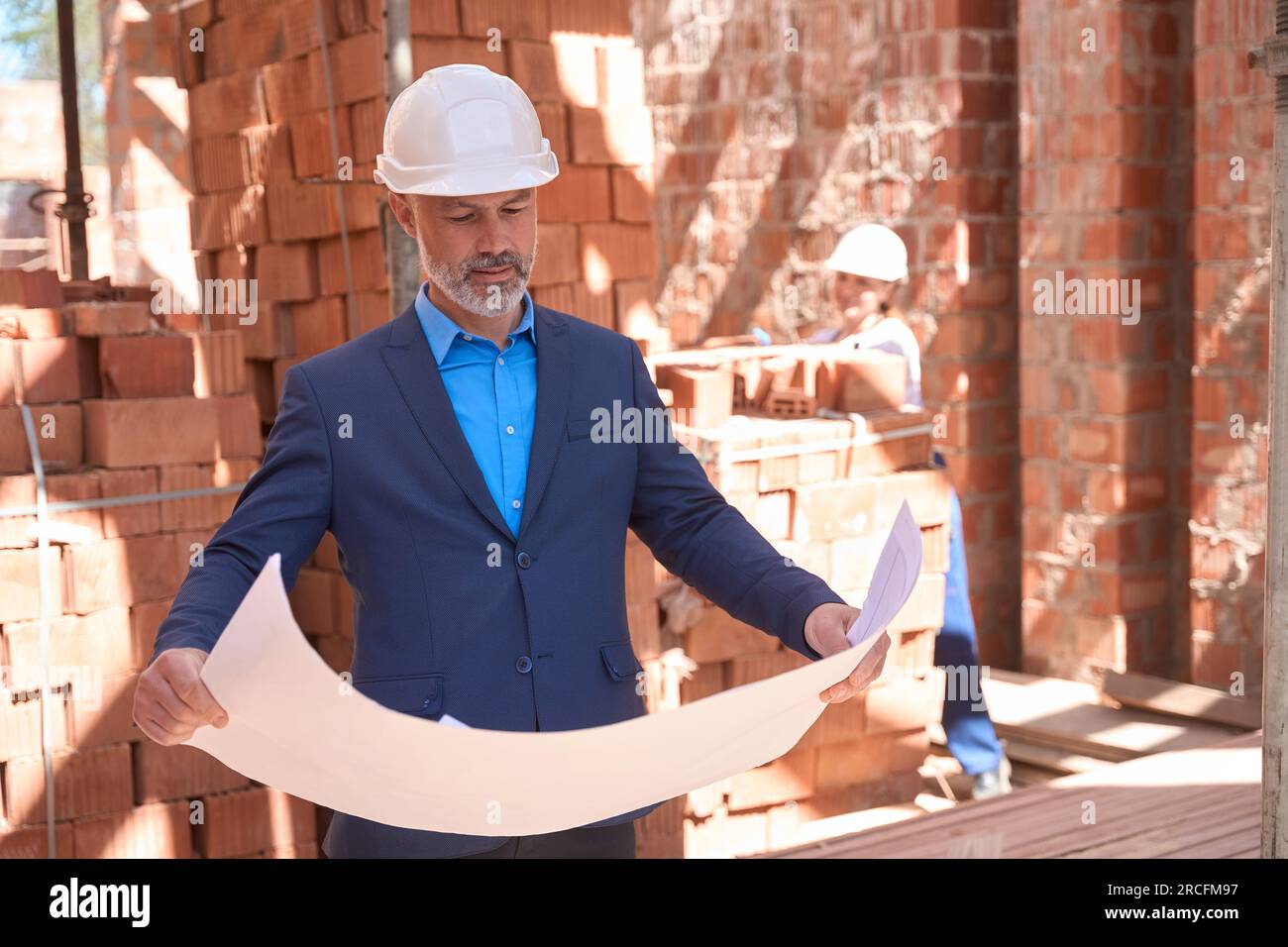 Lead architect in business suit and hardhat looking at building blueprint Stock Photo