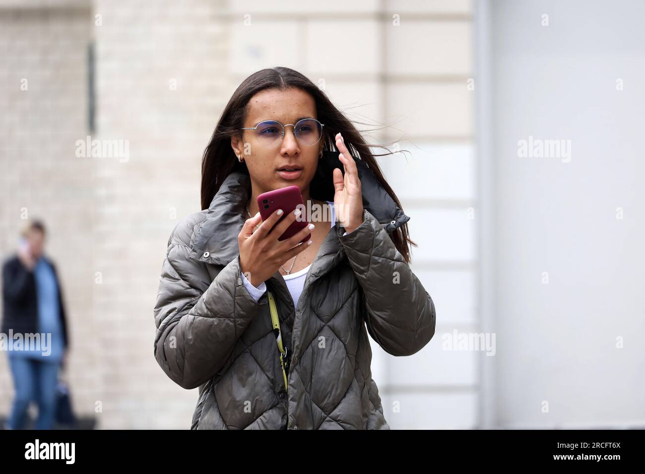 Girl in eyeglasses talking on smartphone using speakerphone while walking down street. Using mobile phone in summer city Stock Photo