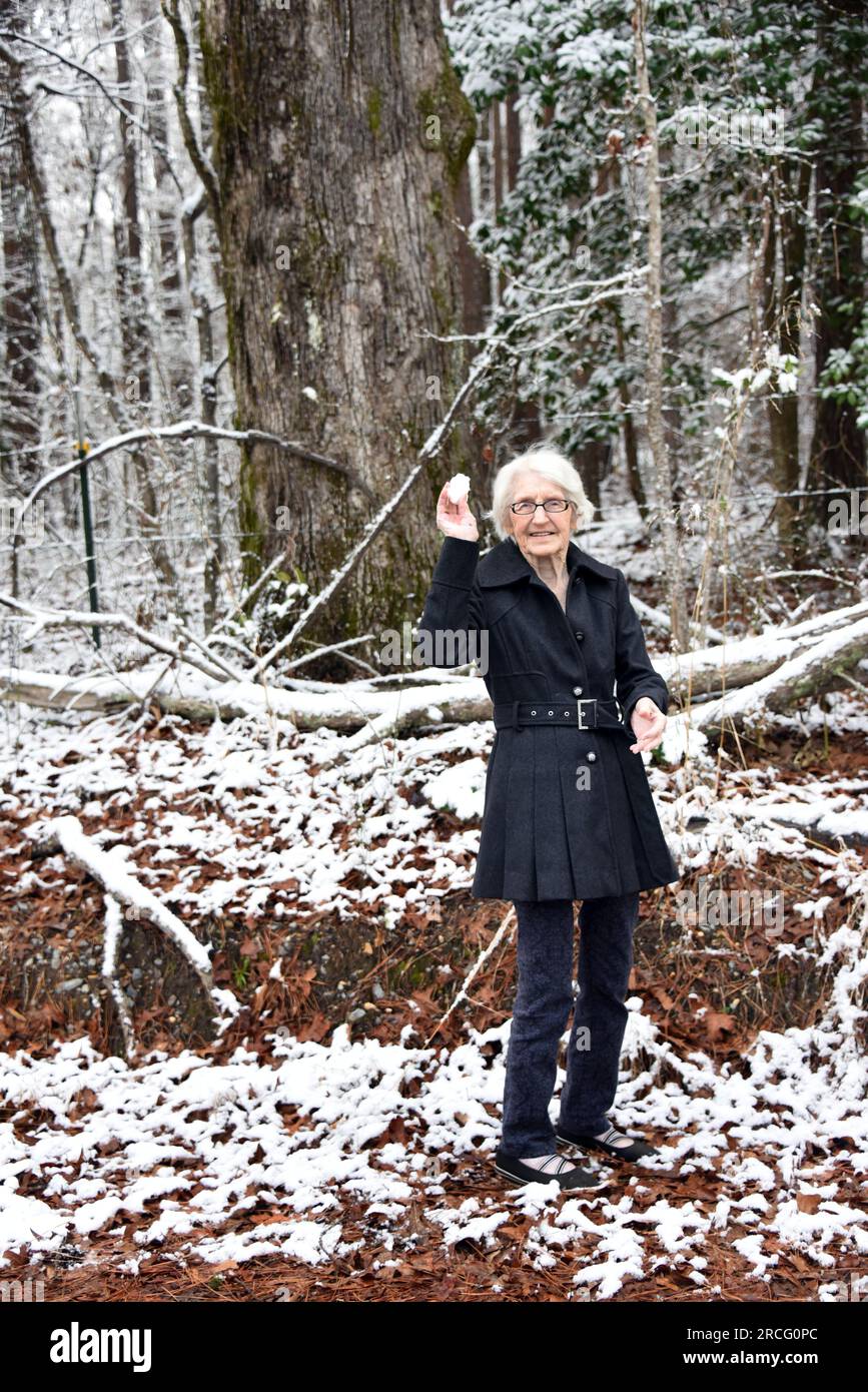 100 year old woman, threatens to start a snowball fight as she holds it in her hand.  She is smiling and standing outside in the snow. Stock Photo