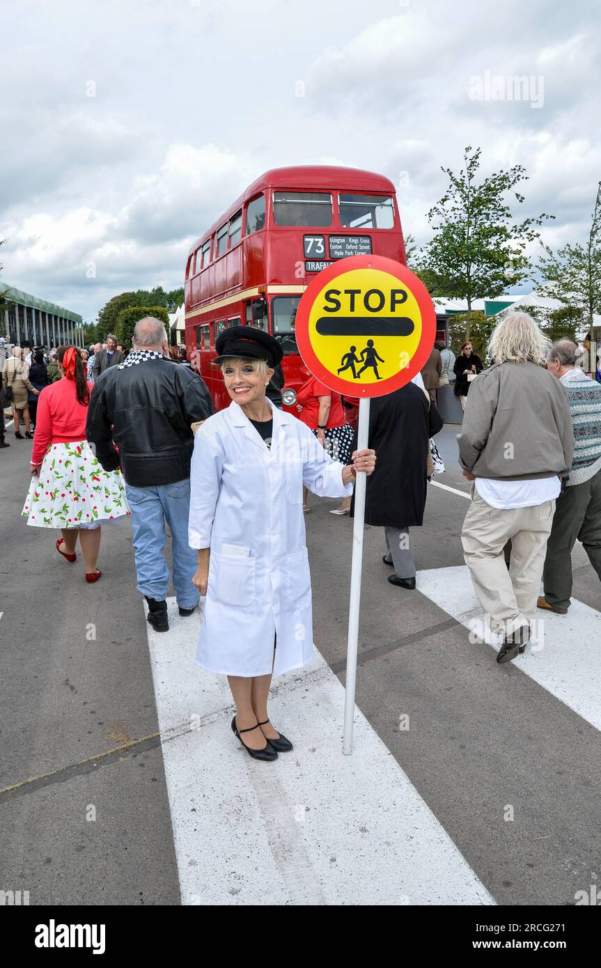 Lollipop lady at the Goodwood Revival retro event. Actor in period crossing guard attire at a zebra crossing with vintage bus and people attending Stock Photo