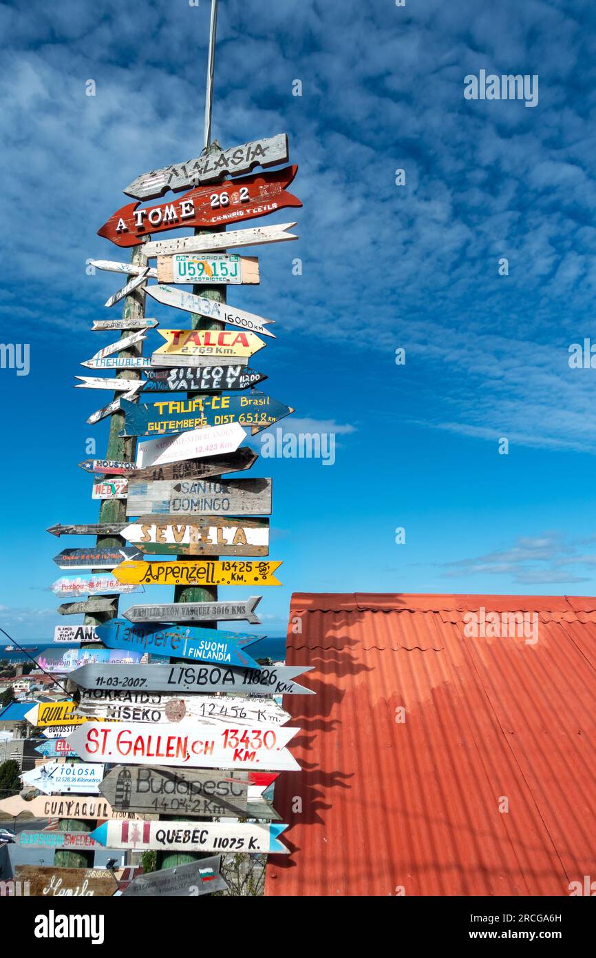 Vertical Arrow Sign Post with World Destination Information Directions by Red Roof against the Blue Sky at Punta Arenas, Chilean Patagonia Stock Photo