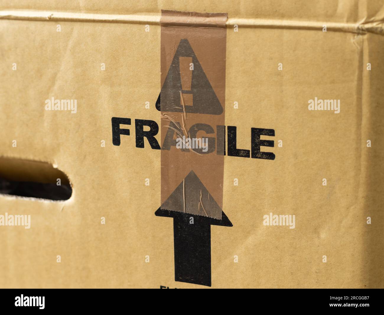Fragile warning on a parcel and a brown tape on it. Sign to prevent careless handling of the package during shipping. Transportation of goods. Stock Photo