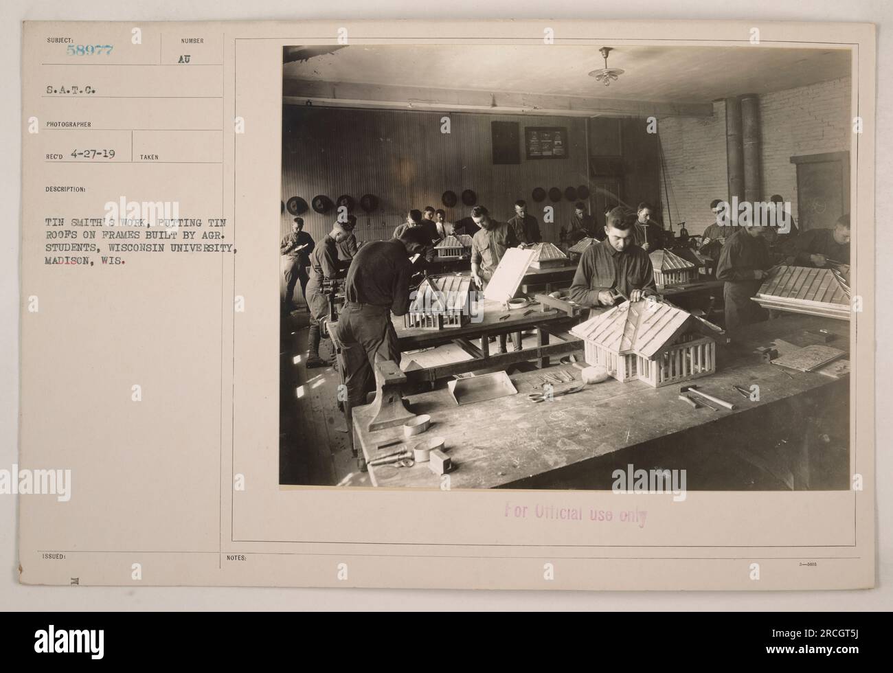 A group of agricultural students from the University of Wisconsin, Madison, are pictured working alongside a tin smith. They are seen putting tin roofs on frames they have built themselves. The photograph is part of a series documenting American military activities during World War I. Stock Photo