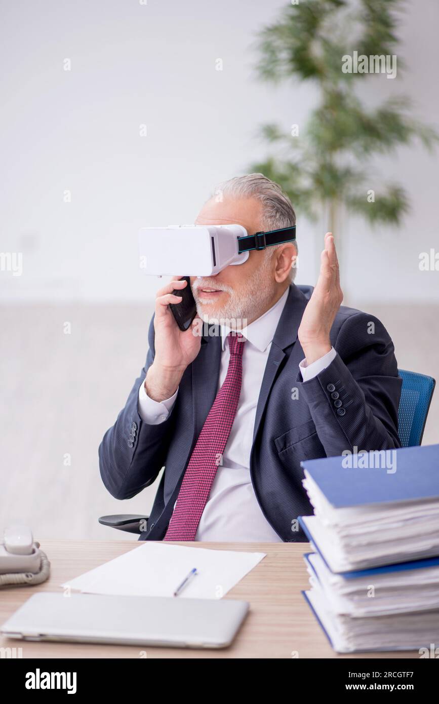 Old employee wearing virtual glasses at workplace Stock Photo