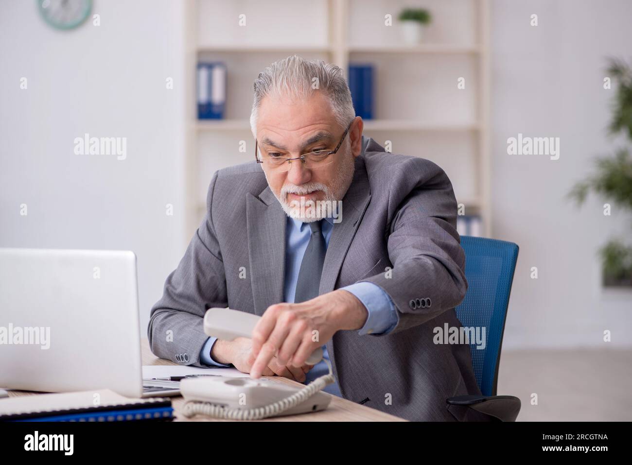Old employee speaking by phone at workplace Stock Photo