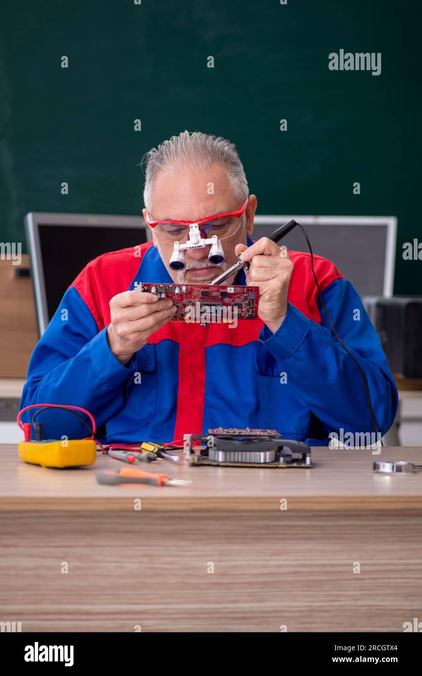 Old male repairman repairing computers in the classroom Stock Photo