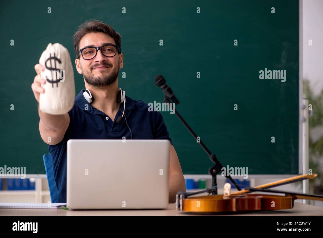 Young music teacher holding moneybag in the classroom Stock Photo