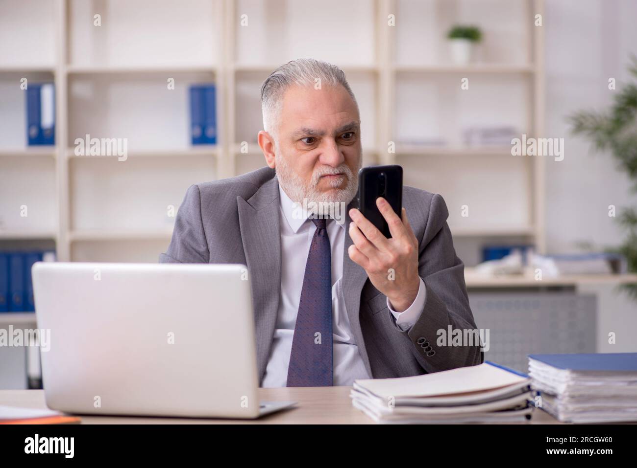Old employee speaking by phone at workplace Stock Photo