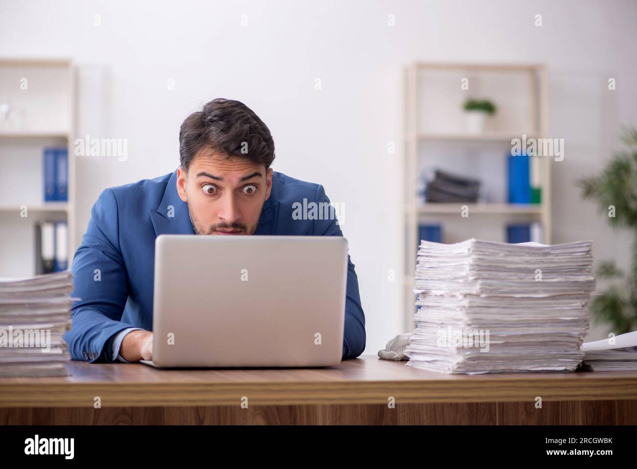 Young employee and too much work at workplace Stock Photo