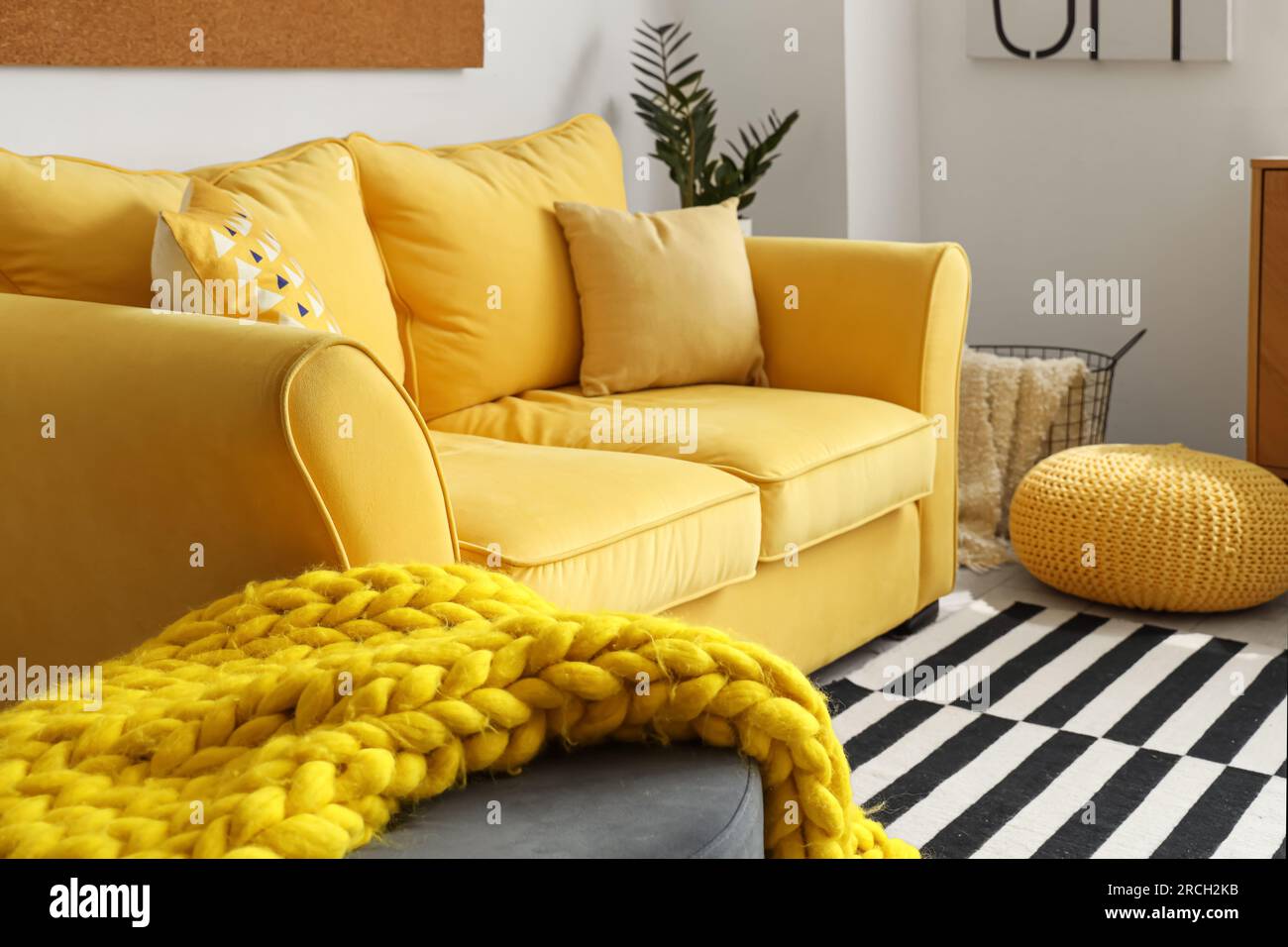 Interior of stylish living room with cozy yellow sofa and soft knitted ...