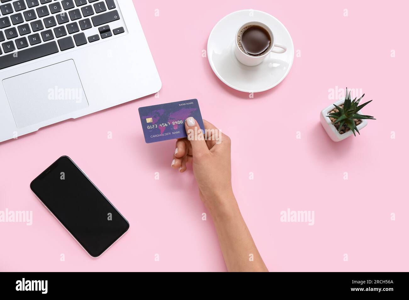Female hand with credit card, cup of coffee and mobile phone on pink background Stock Photo