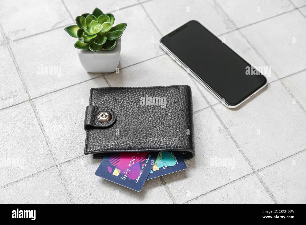 Leather wallet with credit cards, mobile phone and houseplant on white tile background Stock Photo