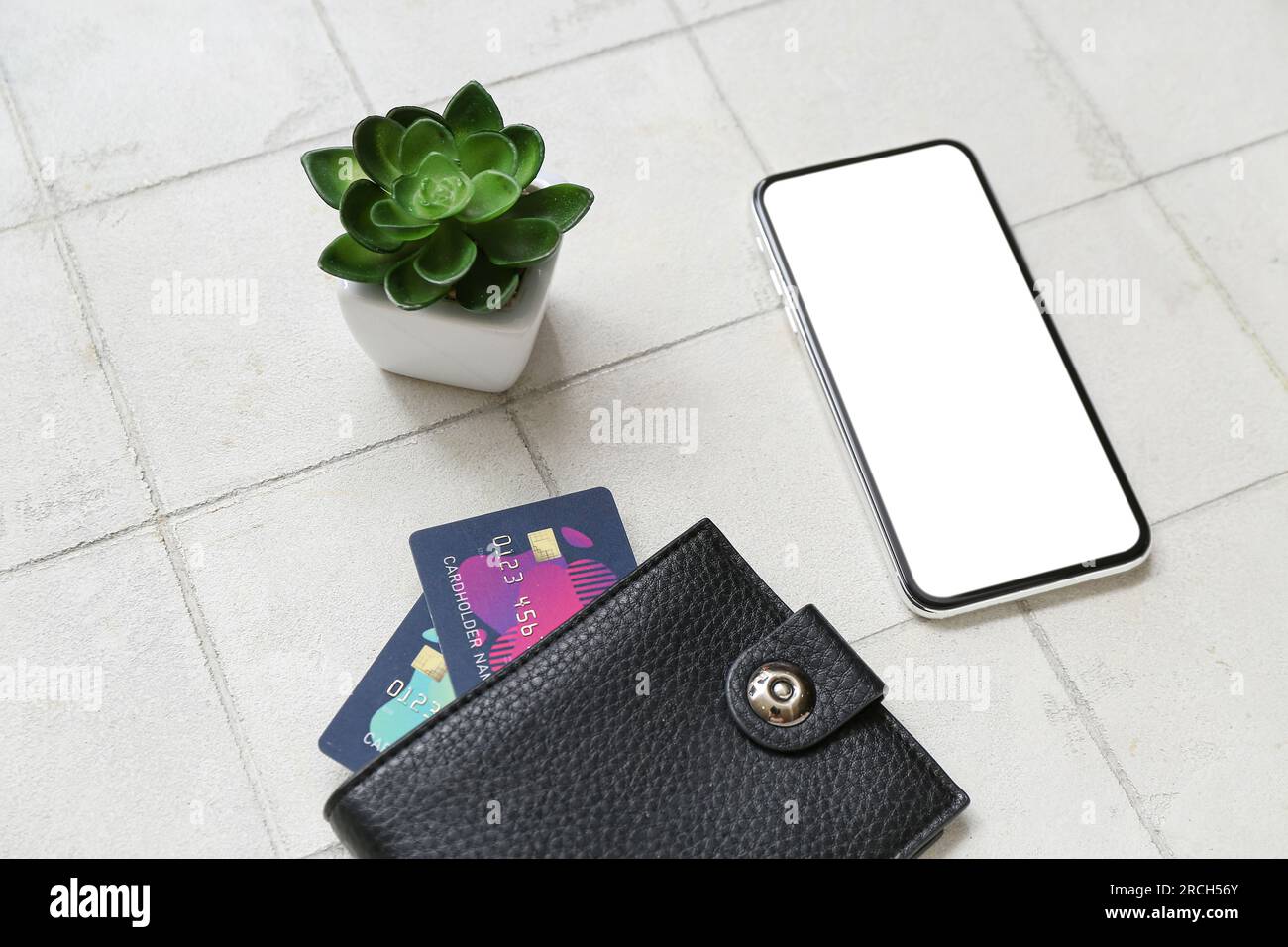 Leather wallet with credit cards, mobile phone and houseplant on white tile background Stock Photo