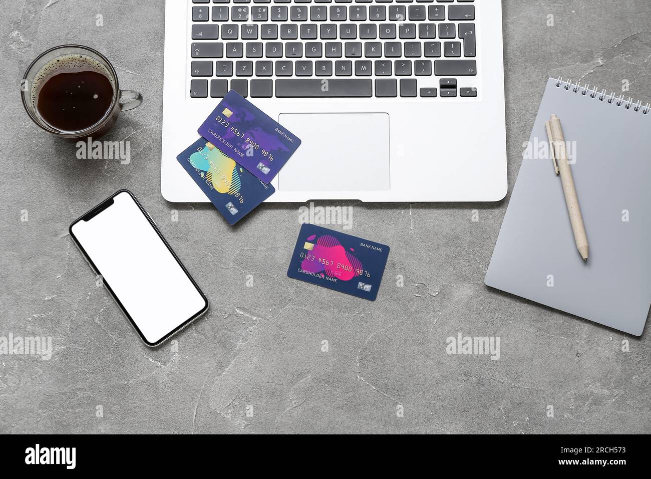 Laptop with credit cards, mobile phone and cup of coffee on grunge grey background Stock Photo