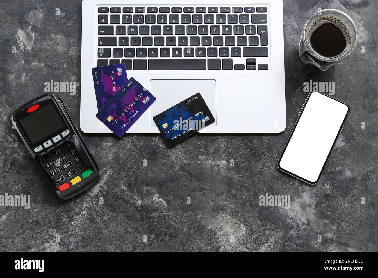 Laptop with payment terminal, mobile phone, credit cards and cup of coffee on grunge black background Stock Photo