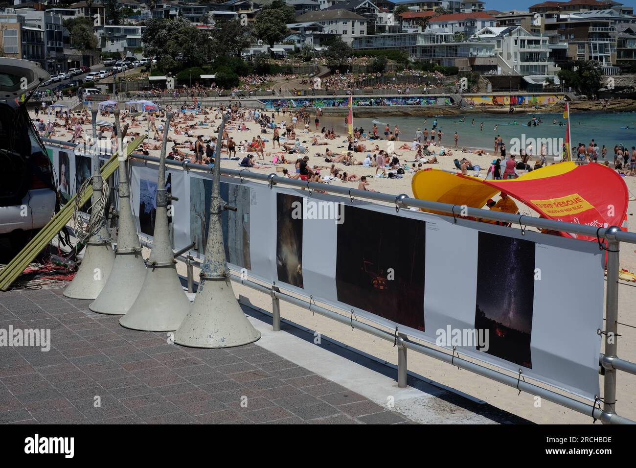 Tannoy speakers on the Bondi beach promenade, people on the beach on a sunny day and the 2022 outdoors head on photography exhibition Stock Photo