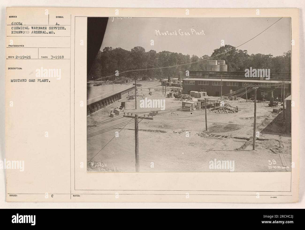 A photograph of a mustard gas plant at Edgewood Arsenal, MD, taken in July 1918. The image shows Symbol Number 60054 A, which is a part of the Chemical Warfare Service. The photograph was received on February 19, 1921. The description notes that this is the Mustard Gas Plant 59, with additional coordinates indicating its location. Stock Photo