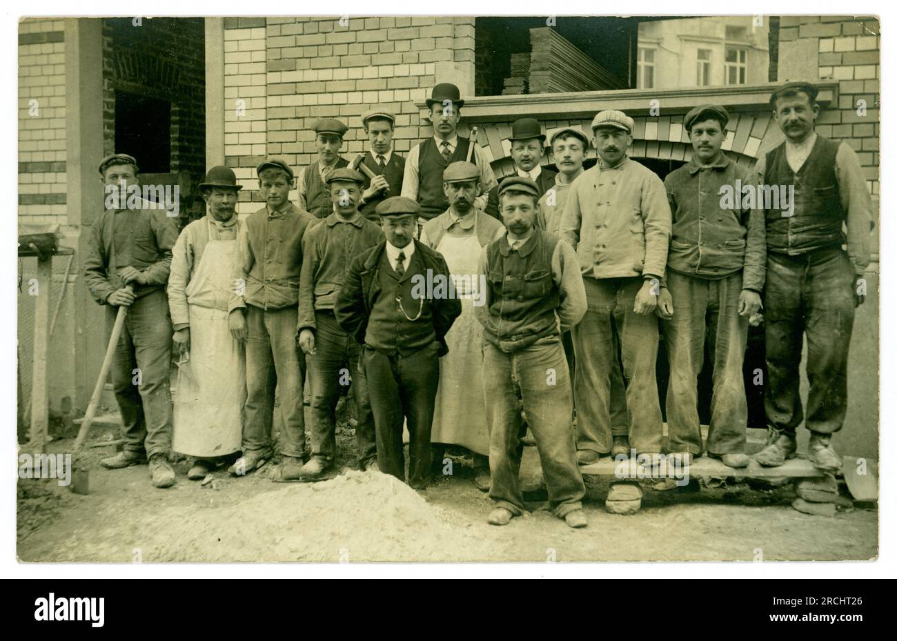 Original and clear 1920's French postcard of a group of builders and bricklayers, one of the men is called Pacha. Lots of characters, France. Stock Photo